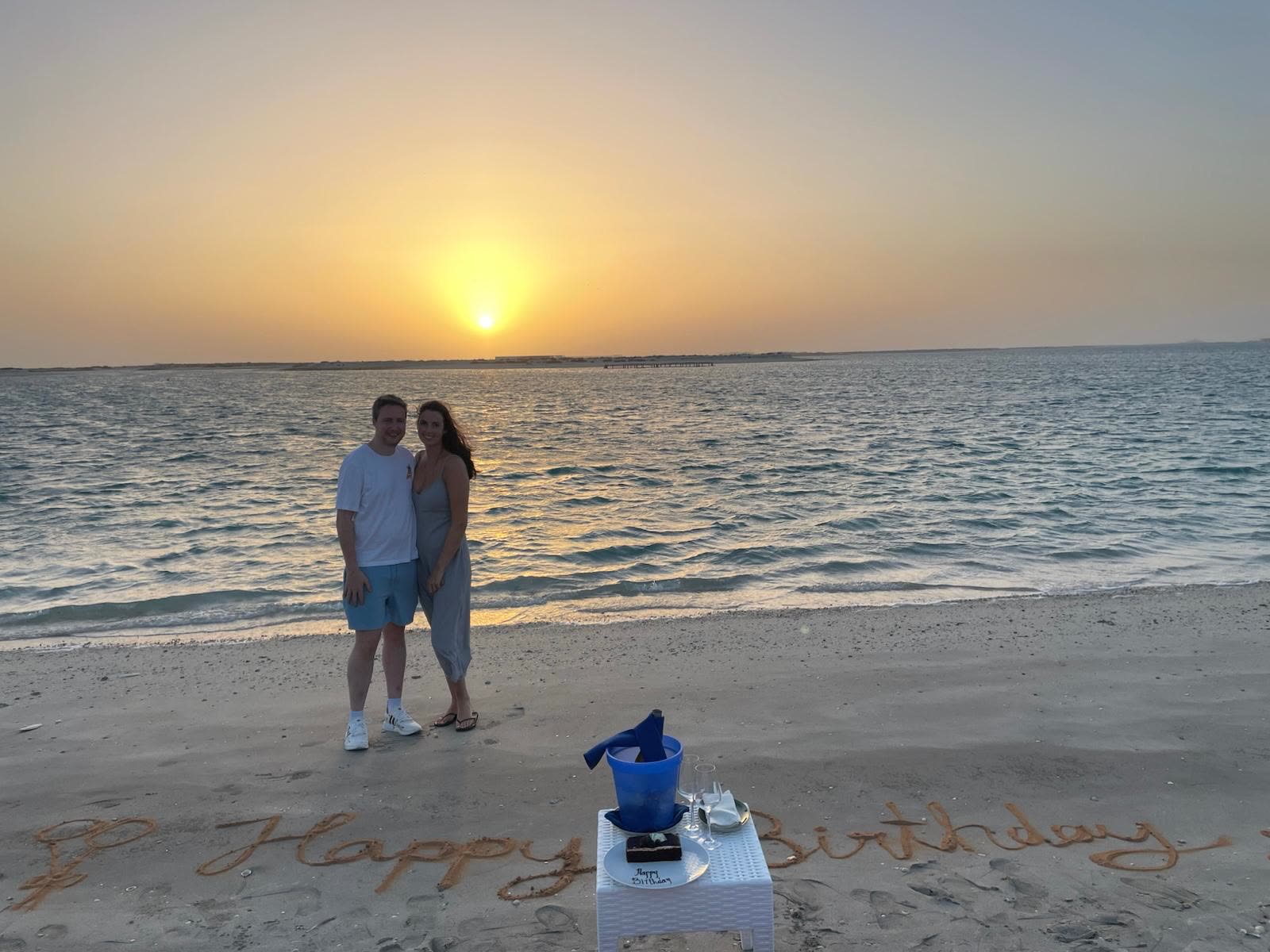 On a beach at sunset with Happy Birthday written in the sand