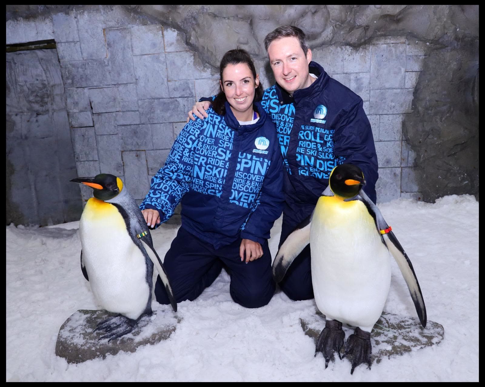 Kneeling in the snow with two king penguins at Ski Dubai